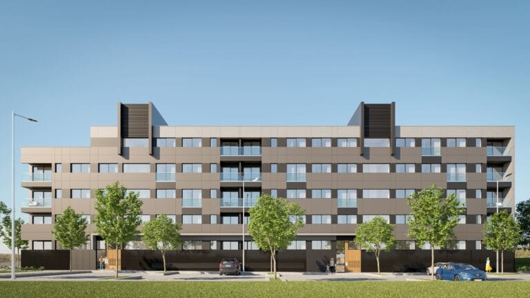 Modern beige apartment building with multiple balconies under a clear blue sky street level with trees and parked cars