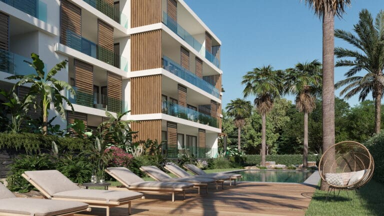Modern residential building with glass balconies beside a pool area and tropical plants