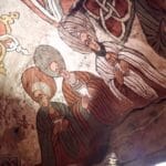 Colorful wall fresco showing several men in striped robes with folded hands in prayer next to a decorative knotwork design