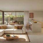 Open plan living room and kitchen with large glass doors opening to a green garden beige sofa and wooden stools at an island