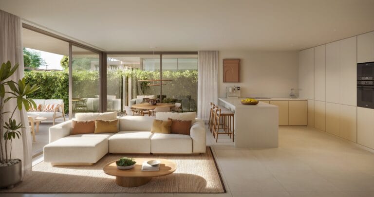Open plan living room and kitchen with large glass doors opening to a green garden beige sofa and wooden stools at an island