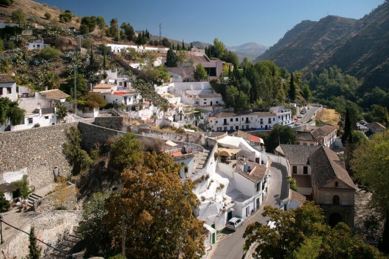 Hillside village with whitewashed houses on terraced slopes a winding road through the valley and distant mountains under a blue sky