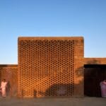 Brick lattice brick wall beneath a clear blue sky two women in pink sarees stand at ground level on opposite sides of the wall