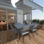 Outdoor wooden deck with a gray dining table and six chairs, beside a sliding glass door to an interior living space on a sunny day?
