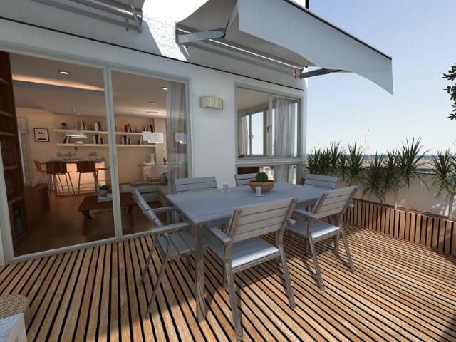 Outdoor wooden deck with a gray dining table and six chairs beside a sliding glass door to an interior living space on a sunny day