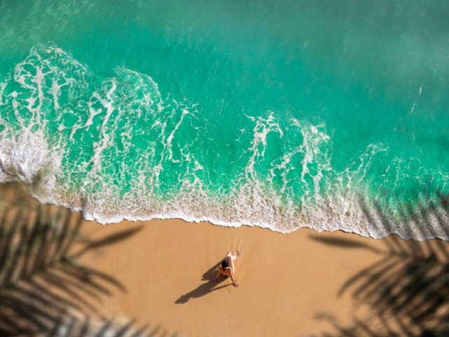 Aerial view of a person sunbathing on a sandy beach with turquoise waves washing ashore