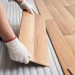Worker wearing gloves fits a wooden floor plank into place during installation on a foam underlayment