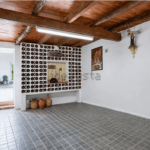 Wine room with wall mounted racks holding hundreds of bottles around a central pass through window and a tiled floor under wooden beams on the ceiling
