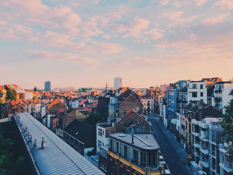 A skyline of dense city rooftops at sunset under a pink tinged blue sky