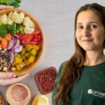 Smiling woman in a green shirt beside a large wooden bowl of colorful vegetable salad