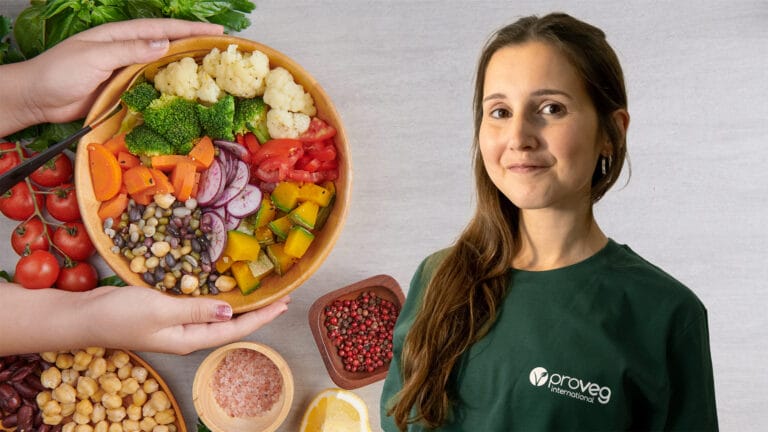 Smiling woman in a green shirt beside a large wooden bowl of colorful vegetable salad
