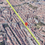 Aerial view of a dense city with a bright yellow diagonal road and a red map pin marking a location along it