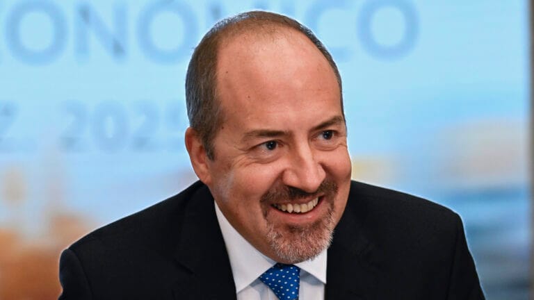 Smiling man in a dark suit and blue tie cropped at shoulders in a bright blurred background portrait style photo