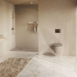 Large beige tinted bathroom with open shower area wall mounted sink and a wall hung toilet by a windowed wall and sheer curtains