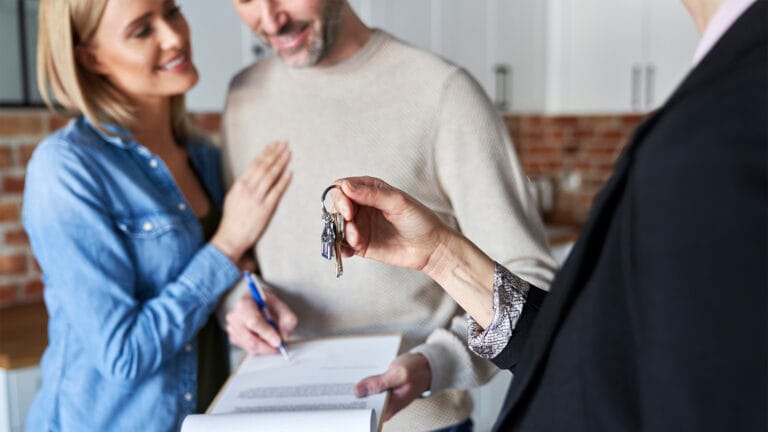 Couple smiles as a real estate agent hands over house keys while they review a contract in the background