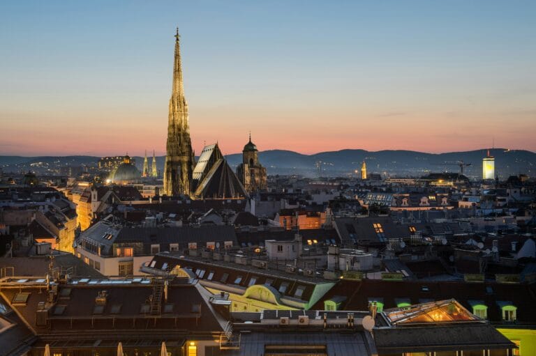 Vienna city skyline at sunset with the tall cathedral spire rising above red tiled rooftops