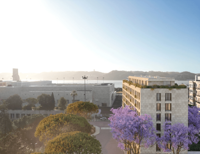 Sunlit urban street with modern beige buildings and purple flowering trees sea visible in the distance under a clear blue sky