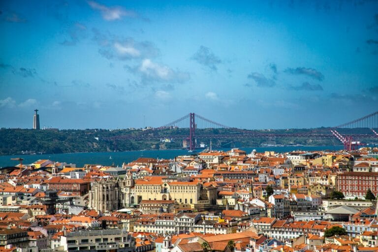 Lisbon cityscape with orange rooftops the Tagus River and the 25 de Abril Bridge Cristo Rei statue on a hill left