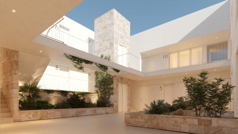 Modern white apartment complex with numbered doors along a sunlit courtyard and stone planters with greenery behind a low wall