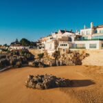 Row of white Mediterranean style houses perched along a rocky coastline under a clear blue sky