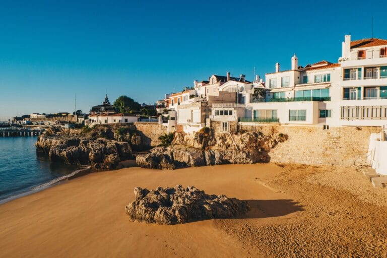 Row of white Mediterranean style houses perched along a rocky coastline under a clear blue sky
