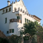 White Mediterranean style villa with arched windows green shutters and a decorative balcony railing against a blue sky