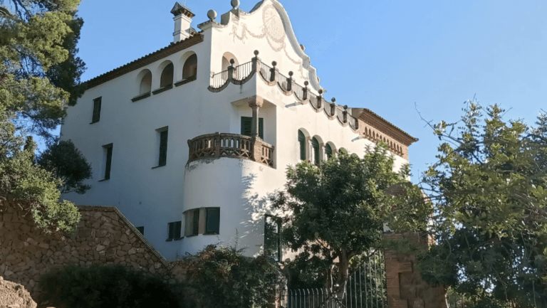 White Mediterranean style villa with arched windows green shutters and a decorative balcony railing against a blue sky