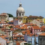 Colorful hillside town with orange tiled roofs and a prominent white domed church tower in the center on a clear day