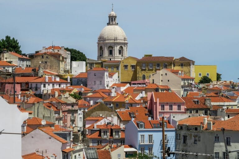 Colorful hillside town with orange tiled roofs and a prominent white domed church tower in the center on a clear day