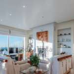 Bright modern living room with white sofas glass coffee table and an ocean view through large sliding doors