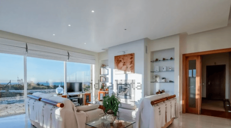 Bright modern living room with white sofas glass coffee table and an ocean view through large sliding doors