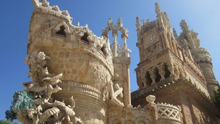 Elaborate stone castle wall with ornate carvings and arches against a clear blue sky