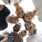 Group of diverse adults and a child smiling into the camera from above forming a circle low angle selfie