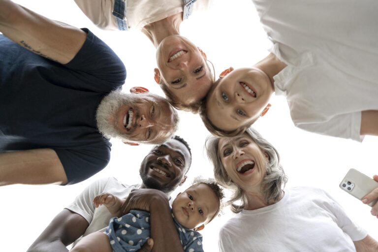 Group of diverse adults and a child smiling into the camera from above forming a circle low angle selfie
