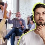 Thinking man in foreground as diverse team raises hands in a bright office meeting behind him