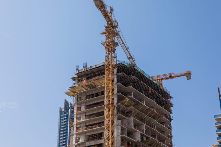Construction site with a tall yellow crane towering over a partially built concrete building against a clear blue sky