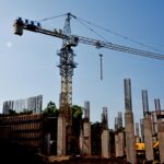 Tower crane at a construction site with concrete columns and exposed steel rebar against a clear blue sky indicating ongoing building work