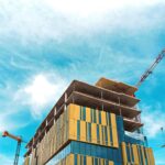 Under construction high rise with yellow and glass facade blue sky and crane on the right