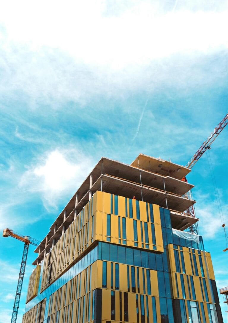Under construction high rise with yellow and glass facade blue sky and crane on the right