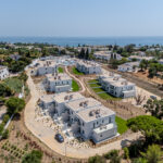 Aerial view of a coastal residential neighborhood with white modern houses and a blue sea on the horizon