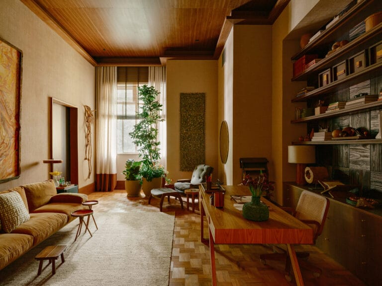 Cozy living room with warm wood ceiling large green plant by a window and dark wood bookshelves filled with books and decor on the right panel