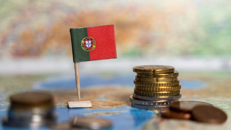 Small Portuguese flag on a toothpick planted in a white base beside a stack of coins on a world map travel money concept