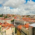 Panoramic cityscape with colorful red tiled rooftops under a bright blue sky and large fluffy clouds