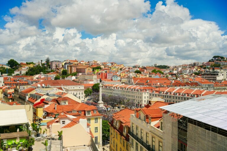 Panoramic cityscape with colorful red tiled rooftops under a bright blue sky and large fluffy clouds