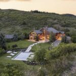 Hillside estate with a two story wooden house illuminated at dusk a rectangular backyard pool and a separate guest cabin among trees