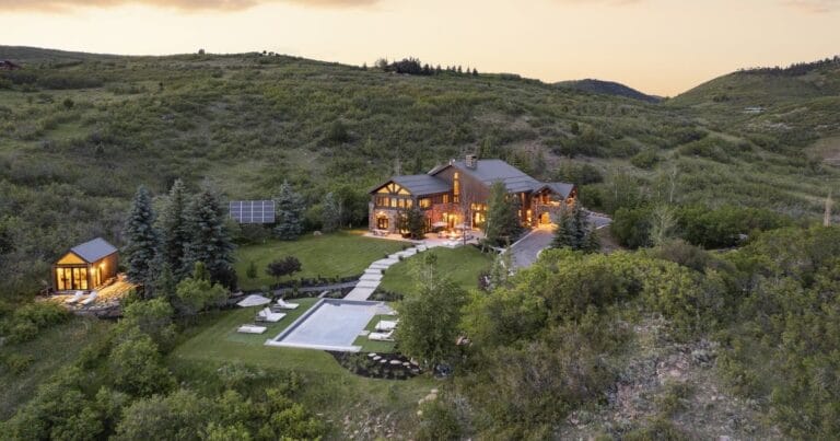 Hillside estate with a two story wooden house illuminated at dusk a rectangular backyard pool and a separate guest cabin among trees