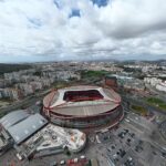 Aerial view of a circular stadium with red and white framing and Emirates signage surrounded by roads lots and city blocks nearby Note good for an overview of the stadium and its surroundings
