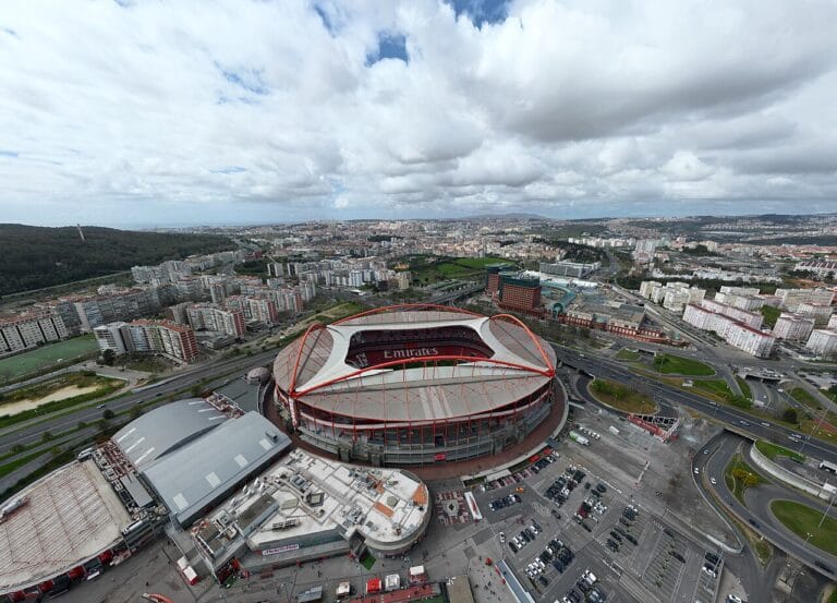 Aerial view of a circular stadium with red and white framing and Emirates signage surrounded by roads lots and city blocks nearby Note good for an overview of the stadium and its surroundings