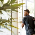 Man with a black backpack about to enter a glass door in a bright lobby