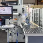 Industrial manufacturing machine with a touchscreen control panel and a conveyor on a factory floor